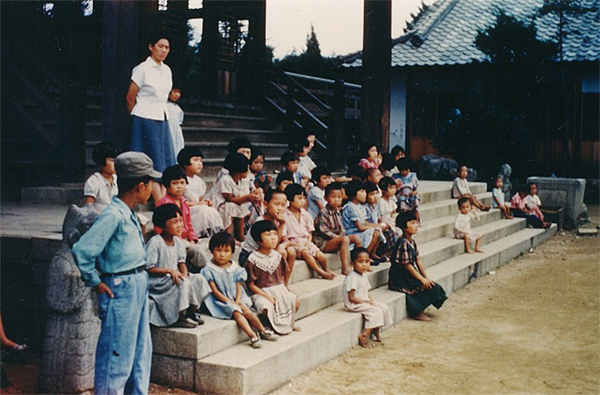 경천애인사의 옛 일본 신사 계단에 앉아있는 고아들. 위에 서 있는 여성은 장시화 목사의 부인이다.