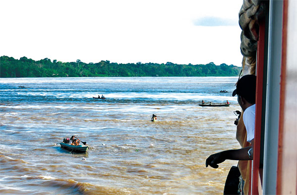 아마존강 주변의 원주민들이 크루즈 승객들이 던져주는 구호물품을 받기 위해 몰려들고 있다. 승객들이 던진 비닐봉지가 강 위에 떠 있다.