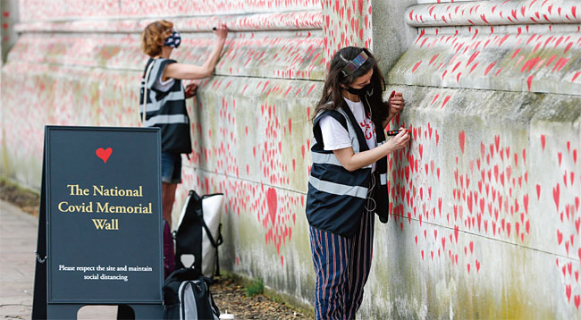 지난 3월 31일 런던 성토머스병원 외곽에 설치된 ‘코로나 희생자 추모 벽’에 자원봉사자들이 하트를 새기고 있다. ⓒphoto 뉴시스