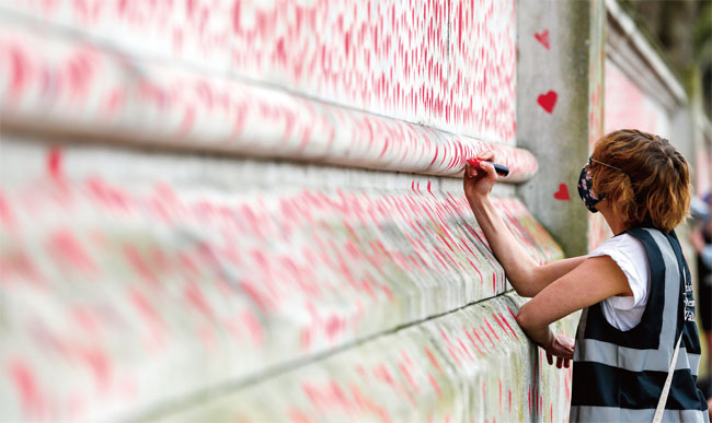 영국의 한 자원봉사자가 지난 4월 런던 성토머스병원 벽에 설치된 코로나19 희생자 추모 벽에 하트 모양을 그려넣고 있다. ⓒphoto 뉴시스