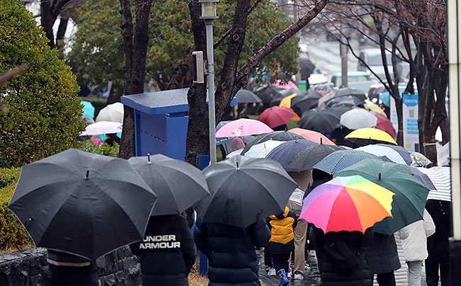 코로나19 확진자가 폭증하고 있는 상황 속에서 12월 16일 부산 남구 보건소 선별진료소를 찾은 시민들이 진단검사를 받기 위해 우산을 쓴 채 길게 줄을 서고 있다. ⓒphoto 뉴시스